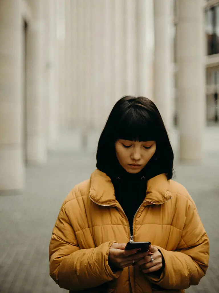 a woman in a yellow coat looking at a cellphone