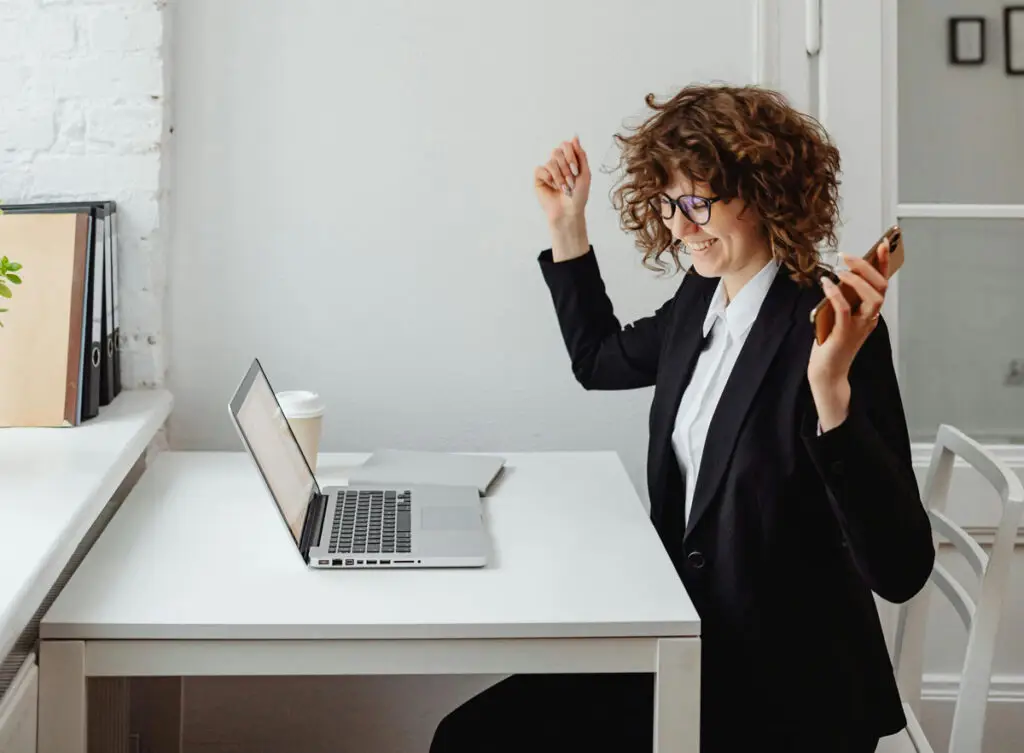 happy business woman sitting a desk with hands raised